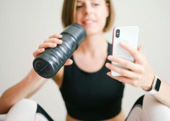 photo of woman holding white smartphone and sports bottle