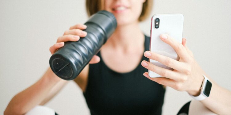 photo of woman holding white smartphone and sports bottle